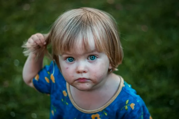 selective focus photography of girl holding her hair playing in the backyard